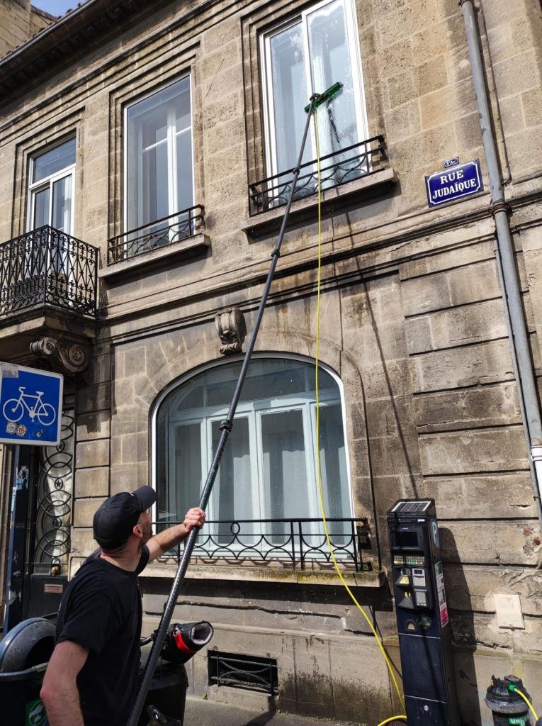 Salarié Leconte Nettoyage nettoyant des vitres en hauteur à Bordeaux à l’aide d’une perche télescopique.